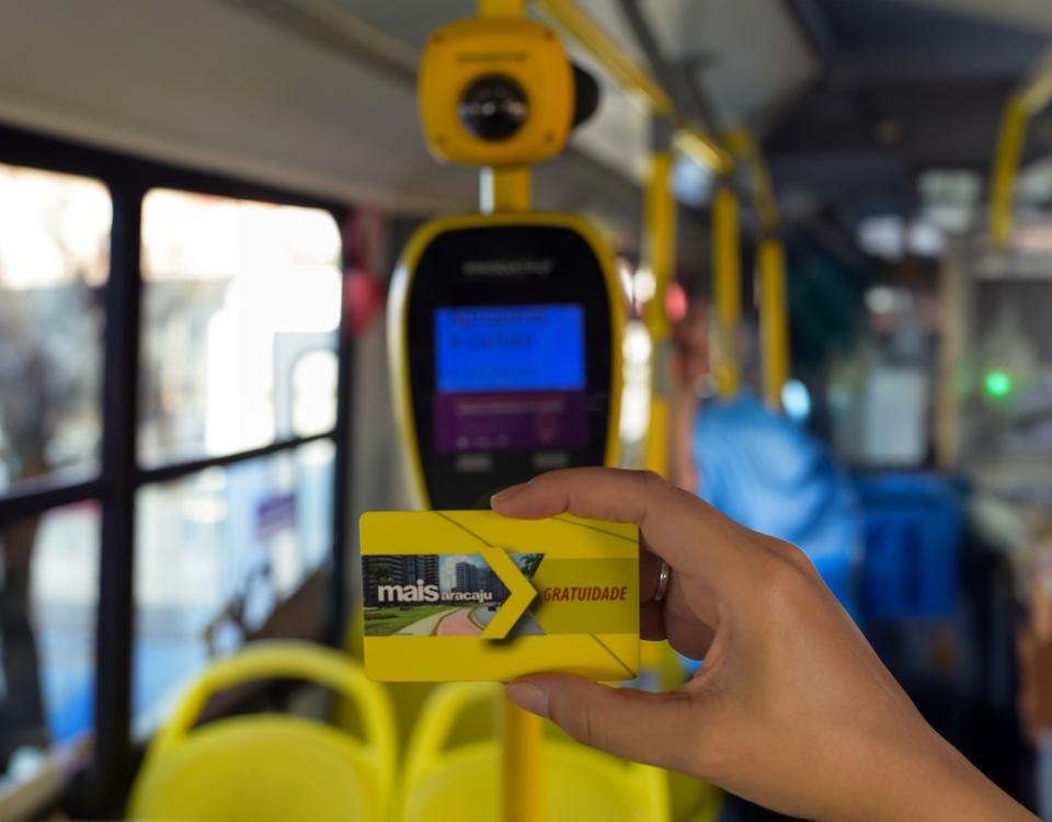 no interior do ônibus mão feminina segura cartão mais aracaju gratuidade em primeiro plano, ao fundo validador e equipamento finger