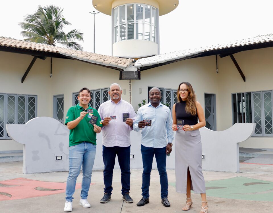 Quatro pessoas em pé, seguram o cartão Mais Aracaju Turista em frente ao Mirante da 13 de Julho
